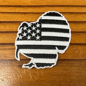 May include: Black and white embroidered patch of a turkey shaped like the American flag.