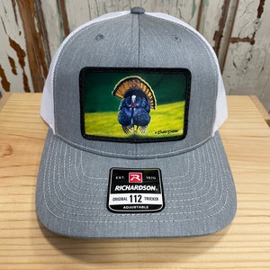 Puede incluir: Un gorro de camionero gris y blanco con un parche que presenta una ilustración de un pavo salvaje colorido. El gorro es ajustable y tiene el texto "Richardson" y "112" en la etiqueta.