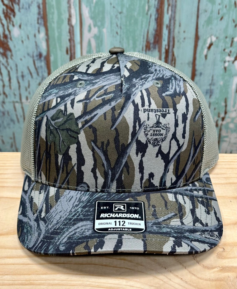 May include: A camouflage trucker hat with a curved peak and mesh back. The hat features a Mossy Oak Treestand pattern and a Richardson patch. The hat is adjustable and has a button on top.
