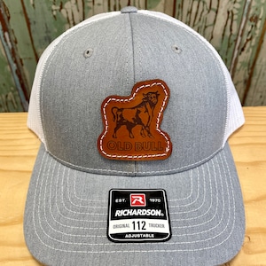 May include: A grey and white trucker hat with a brown leather patch featuring a bull silhouette and the text "Old Bull". The hat has a black label with the text "Richardson" and "Original 112 Trucker Adjustable".