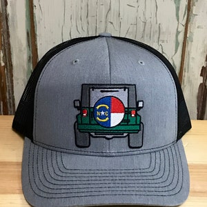 May include: Gray and black trucker hat with an embroidered design of a green Jeep with a North Carolina license plate. The Jeep is facing away from the viewer.