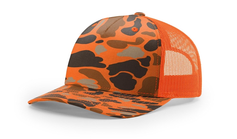 May include: Orange and brown camouflage baseball cap with a mesh back. The cap features a curved brim and a classic trucker hat design. The camouflage pattern includes shades of brown, tan, and orange.