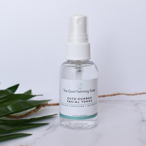 May include: A clear glass bottle with a white spray top containing a cucumber facial toner. The bottle is labeled "The Goat Fetching Soap" and "Cute-Cumber Facial Toner".