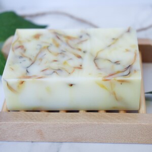 May include: A bar of natural soap with a swirl pattern of light brown and white. The soap is sitting on a wooden soap dish.