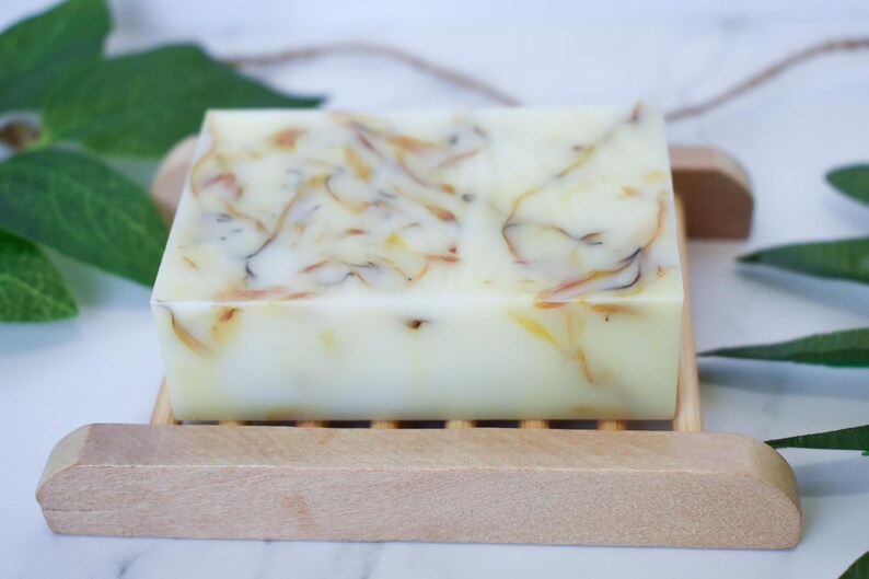 May include: A bar of natural soap with a swirl pattern of light brown and white. The soap is sitting on a wooden soap dish.