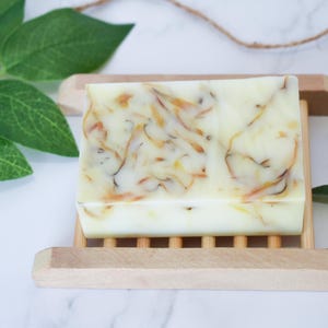 May include: A white bar of soap with swirls of orange and yellow. The soap is on a wooden soap dish.