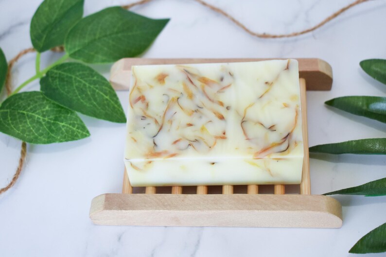 May include: A white bar of soap with swirls of orange and yellow. The soap is on a wooden soap dish.