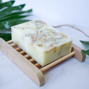 May include: A white bar of soap with dried flowers and herbs embedded in it. The soap is sitting on a wooden soap dish.