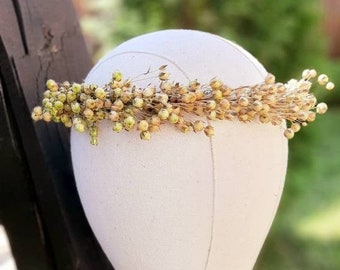 May include: A dried flower crown with small, light brown and green flowers. The crown is displayed on a white fabric mannequin head.