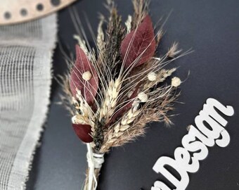 May include: A small, dried flower bouquet with burgundy leaves, wheat, and other dried elements, tied with white string. The bouquet is set against a dark background with the white text "TnDesign" and a portion of a clock face.