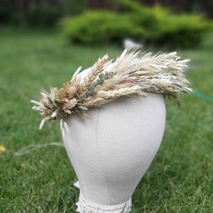 Könnte beinhalten: Eine Trockenblumenkrone aus Weizen und anderen Gräsern. Die Krone befindet sich auf einem weißen Mannequin-Kopf und ist vor einem grünen Gras-Hintergrund platziert.
