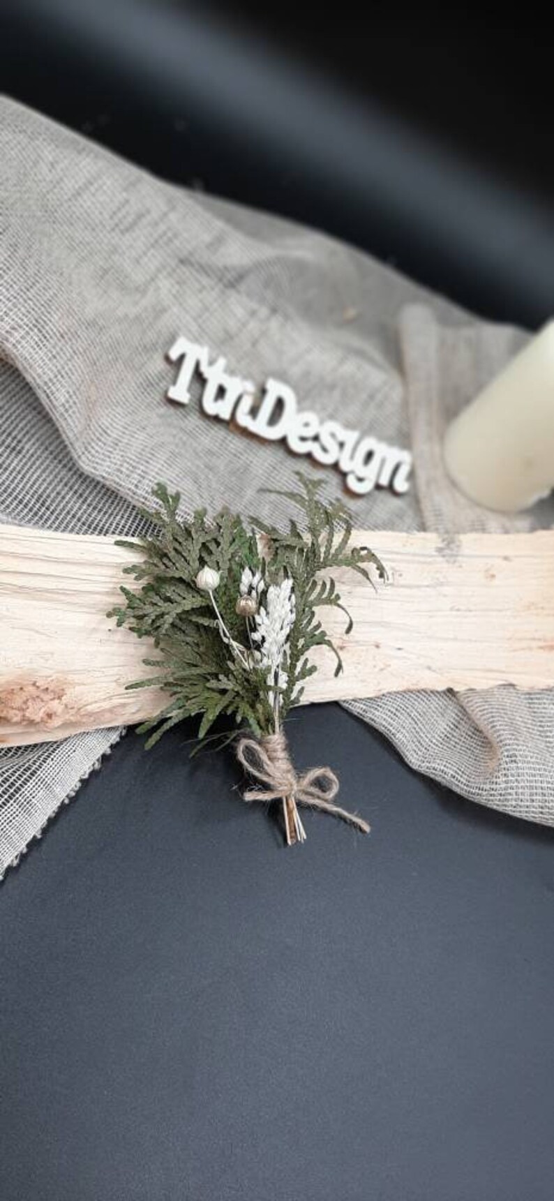 May include: A small bouquet of dried greenery and white flowers tied with twine. The bouquet is sitting on a piece of wood with a burlap background.