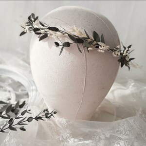 May include: A delicate floral crown with white and green dried flowers. The crown is made with eucalyptus leaves and small white flowers.