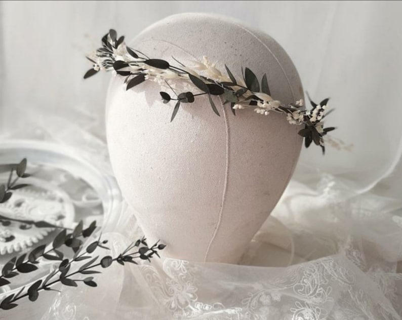 May include: A delicate floral crown with white and green dried flowers. The crown is made with eucalyptus leaves and small white flowers.