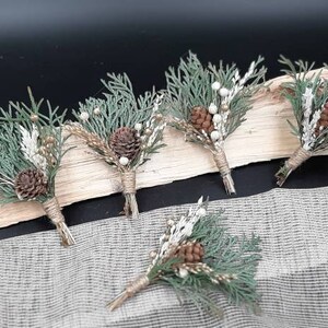 May include: Five small bouquets of greenery, pine cones, and white berries tied with twine. The bouquets are arranged on a wooden surface.