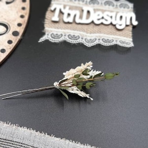 May include: A silver hair pin with a small bouquet of dried white and green flowers attached.
