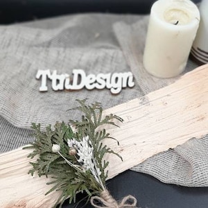 May include: A small bouquet of dried greenery and white flowers tied with twine. The bouquet is sitting on a piece of wood with a white sign that says "TtnDesign".