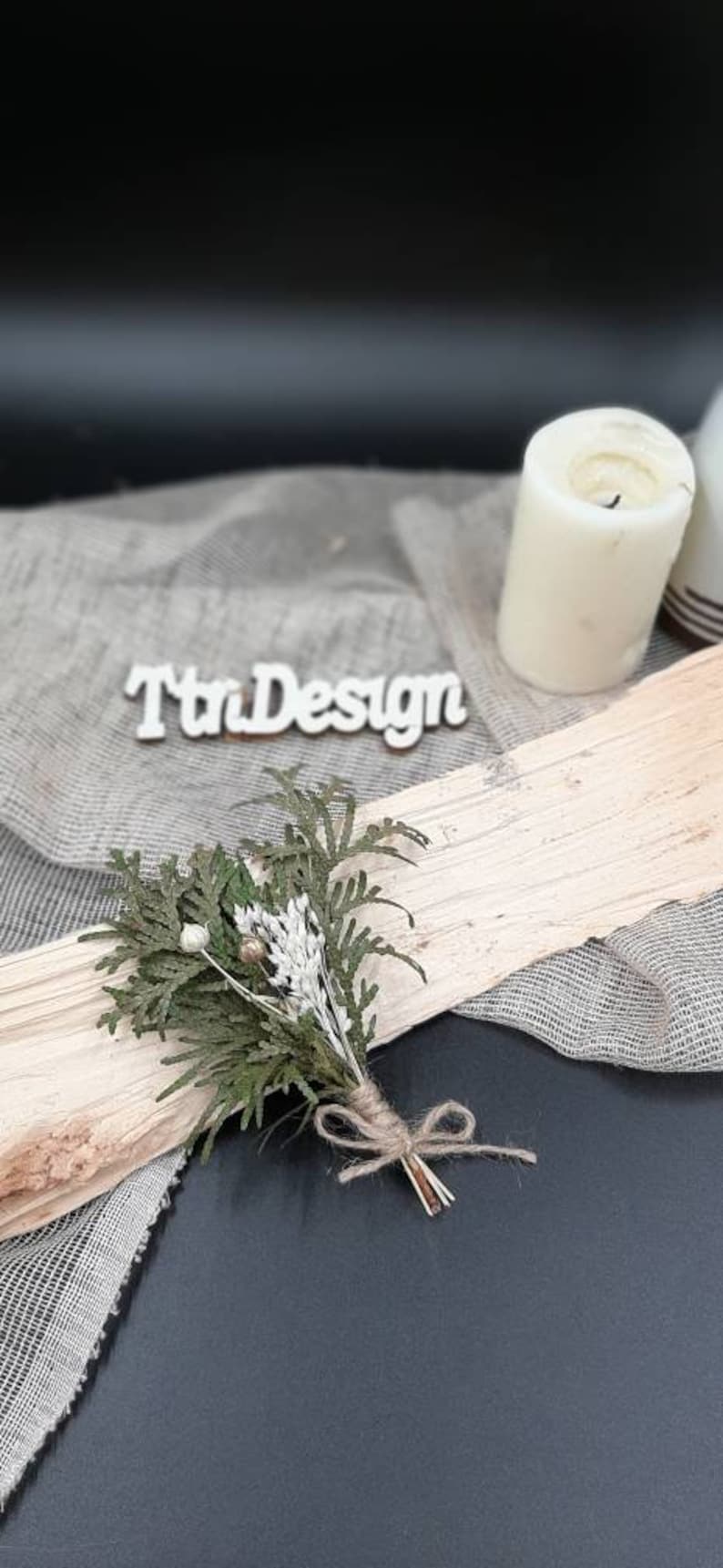 May include: A small bouquet of dried greenery and white flowers tied with twine. The bouquet is sitting on a piece of wood with a white sign that says "TtnDesign".