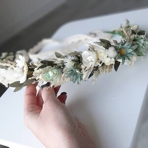 May include: A white and green floral crown with dried flowers and greenery. The crown is made with a white ribbon.
