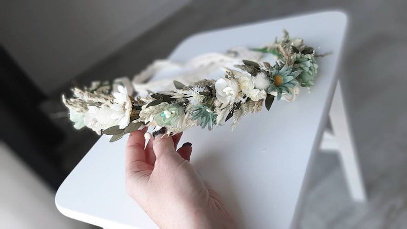 May include: A white and green floral crown with dried flowers and greenery. The crown is made with a white ribbon.