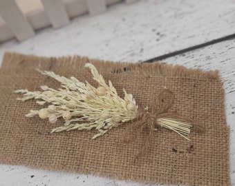 May include: A small bouquet of dried white flowers tied with twine and placed on a brown burlap surface.
