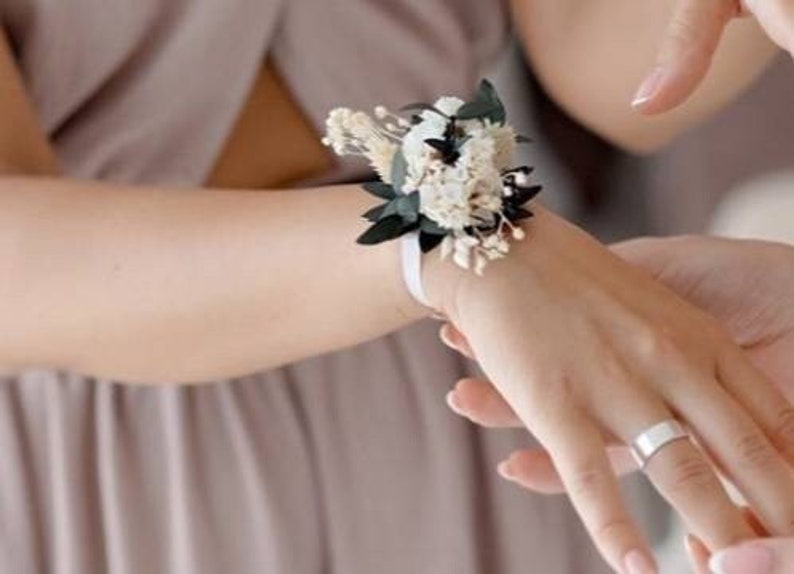 May include: A white and green dried flower wrist corsage with a white satin ribbon.