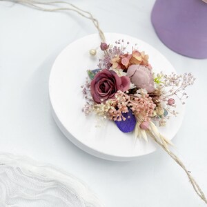 Op de afbeelding: Een klein boeket gedroogde bloemen in roze en paarse tinten, vastgebonden met touw, op een witte achtergrond.