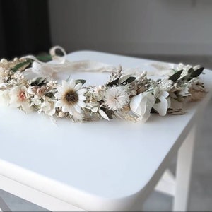 May include: A white and cream floral crown with dried flowers and greenery. The crown is made with a variety of flowers, including daisies, baby's breath, and eucalyptus.