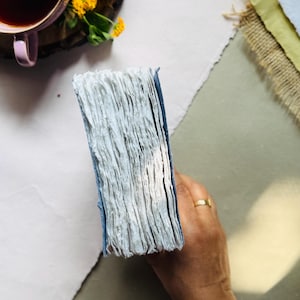 May include: A set of three ceramic mugs with a speckled, matte finish. Each mug features a different color: light blue, cream, and gray. The mugs have a simple, modern design and a comfortable handle. Perfect for coffee or tea.