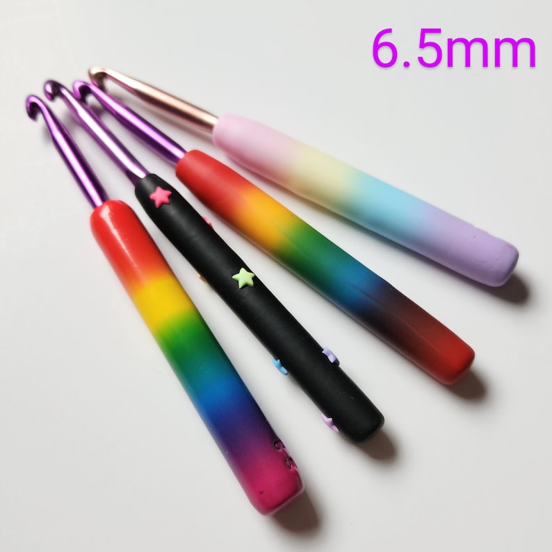 May include: Set of five rainbow crochet hooks, each with a different color gradient and decorated with small stars. The hooks are 6.5 mm in size.