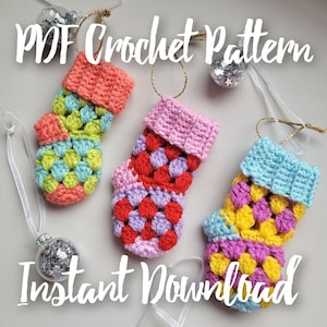 May include: Three crocheted Christmas stocking ornaments in different color combinations. The stockings are pink and red, pink and purple, and blue and yellow. The ornaments are hanging from white ribbon. The text "PDF Crochet Pattern Instant Download" is written on the image.