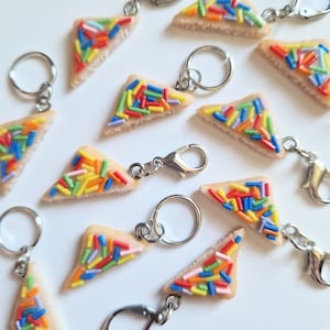 Puede incluir: Un conjunto de 10 llaveros hechos a mano de arcilla polimérica con forma de rebanadas de pan con chispas de arcoíris. Cada llavero tiene un anillo de metal plateado y un broche de langosta.