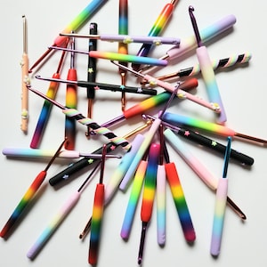 May include: A collection of colorful crochet hooks with rainbow, black and white, and pastel gradient designs. The hooks are made of plastic and have a variety of sizes.