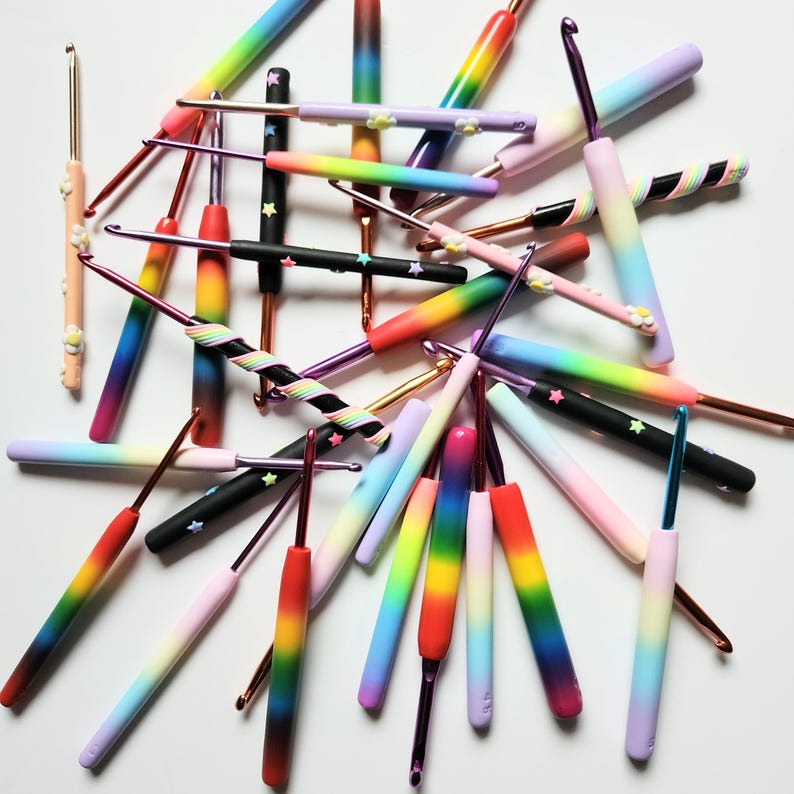 May include: A collection of colorful crochet hooks with rainbow, black and white, and pastel gradient designs. The hooks are made of plastic and have a variety of sizes.