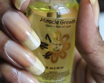 May include: A clear glass bottle with a yellow liquid inside. The bottle is labeled "Miracle Growth Cuticle & Nail Oil Refill" with a gold flower design and the text "Beauty & Bath". The bottle is being held by a hand with long, clear nails.