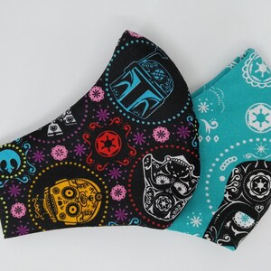 May include: Two fabric face masks with a black background and colorful patterns. One mask has a turquoise background with white star wars symbols and the other has a black background with colorful skulls and star wars symbols.