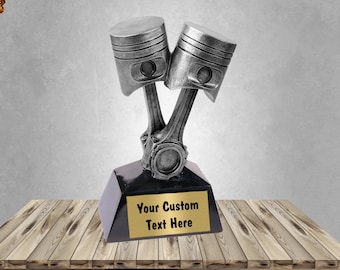 May include: Silver trophy with two pistons and connecting rods. The base is black with a gold plate that says "Your Custom Text Here".