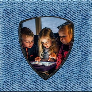 Peut inclure: Trois enfants regardent attentivement une tablette, probablement en train de jouer. L'image est encadrée dans un motif denim. Leurs visages sont éclairés par la lumière de l'écran, créant une atmosphère de concentration. La scène suggère une activité partagée.