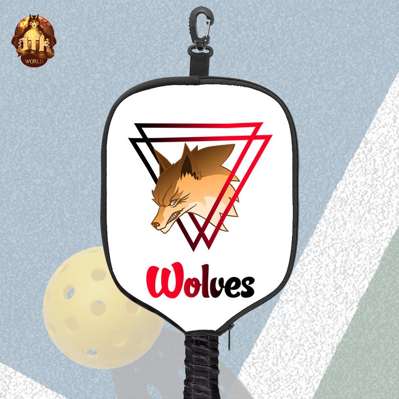 Puede incluir: Raqueta de pickleball blanca con mango negro y correa negra. La raquette tiene un gr&aacute;fico de lobo rojo y negro con la palabra "Wolves" en letras rojas.