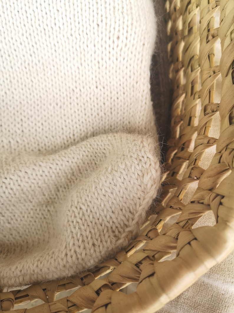 May include: A close-up of a woven wicker basket with a cream-colored knitted blanket draped over the edge.