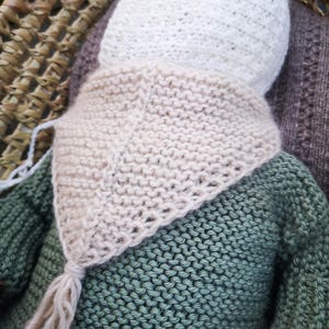 Puede incluir: Un conjunto de bebé tejido a mano, que incluye un gorro blanco, una bufanda beige con borla y un suéter verde. El conjunto está hecho de hilo suave, ideal para un recién nacido. El conjunto se muestra en una cesta tejida.
