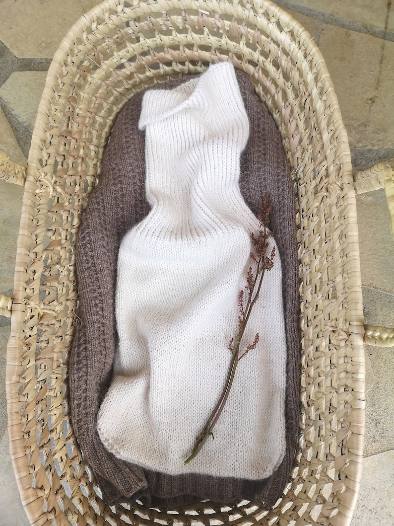 May include: A white knitted turtleneck sweater with a brown knitted sweater underneath, both folded and placed in a woven basket.