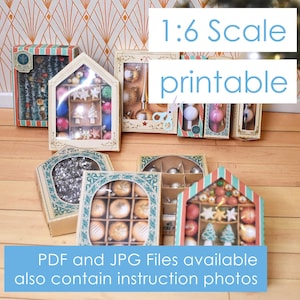Op de afbeelding: Een set van 1:6 schaalbare, printbare kerstversieringen in verschillende stijlen, waaronder een boom, een ster en een bel. De versieringen zitten in dozen met een feestelijk ontwerp. De tekst "1:6 Scale printable" is zichtbaar in de afbeelding.