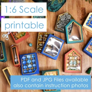 Op de afbeelding: Een set van 1:6 schaalbare, printbare kerstversieringsdozen. De dozen zijn gemaakt van karton en zijn versierd met verschillende kleuren en patronen. De dozen zijn ontworpen om kleine kerstversieringen te bevatten, zoals glazen ballen, sterren en bellen. De dozen zijn ook versierd met de tekst "1:6 Scale printable".