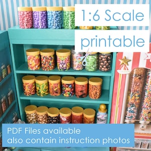 Pode incluir: Uma exposição de loja de doces em miniatura com potes de doces coloridos e o texto "1:6 Scale printable". A exposição inclui uma prateleira azul com vários doces em potes e tubos. O texto "PDF Files available also contain instruction photos" também é visível.
