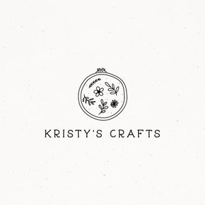 May include: A minimalist logo for "Kristy's Crafts" featuring a circular embroidery hoop with floral and leaf designs. The text "KRISTY'S CRAFTS" is centered below the hoop in a simple, clean font. The background is a speckled off-white.