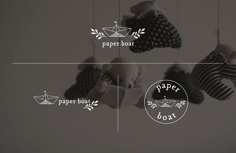 May include: A grayscale image featuring a paper boat logo with the text "paper boat". The logo is displayed in multiple variations, including a circular design and a linear design. The background includes hanging stuffed animals.