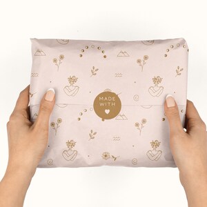 May include: A pink and brown paper package with a repeating pattern of flowers, moons, and mountains. The package is sealed with a brown sticker that says "MADE WITH" and a heart.