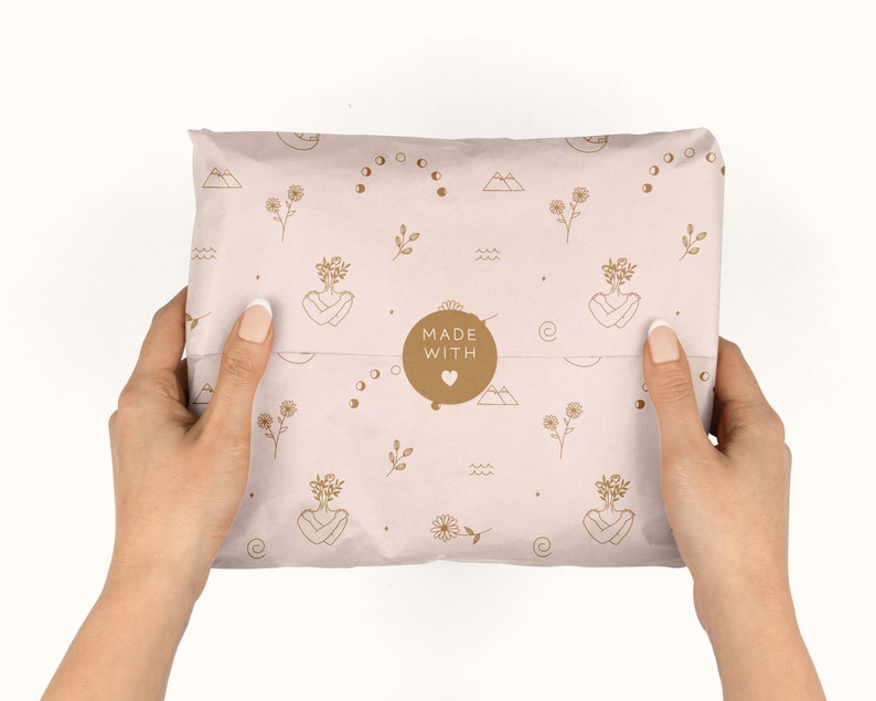 May include: A pink and brown paper package with a repeating pattern of flowers, moons, and mountains. The package is sealed with a brown sticker that says "MADE WITH" and a heart.