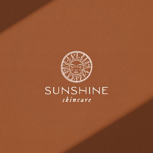 Puede incluir: Un sol blanco con una cara dentro de un c&iacute;rculo con un borde decorativo. El texto "SUNSHINE skincare" est&aacute; debajo del sol.